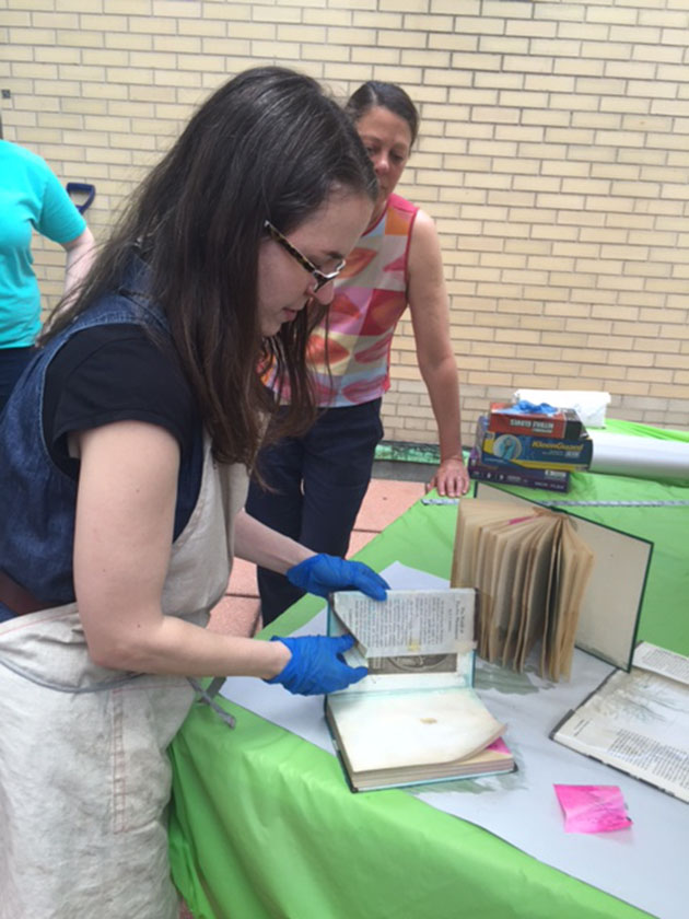 Doreen Pastore looks on as Book Conservator Christina Amato removes a wet dust jacket. 